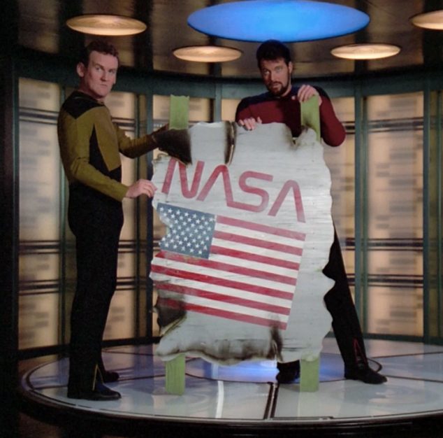O'Brien y Riker transportan destrozo de nave con la marca antigua de la NASA. 
