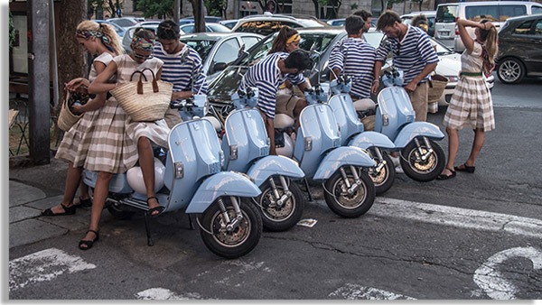 foto con varios jóvenes vestidos como en los años 50, con motos azules de la época