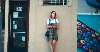 Girl in plaid overalls leans against wall.